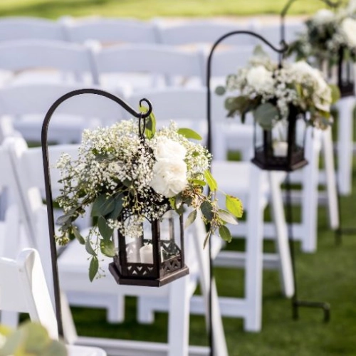 A row of white chairs with flowers in them.