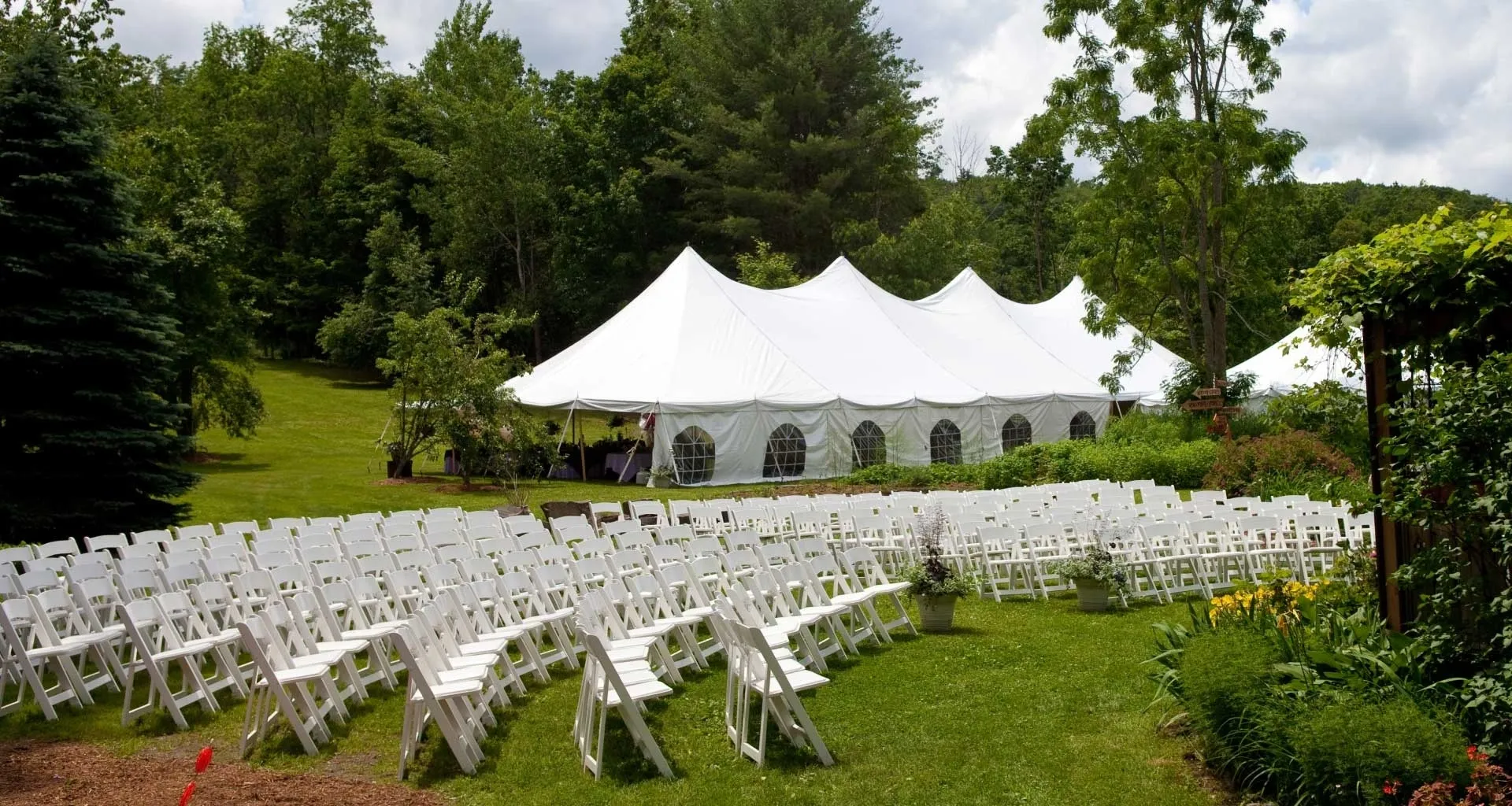 A large white tent with many chairs in the grass.